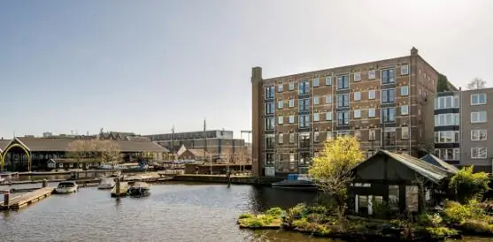 Uitzicht op de Hoogte Kadijk in Amsterdam met een historisch pakhuis aan het water en aangemeerde bootjes.